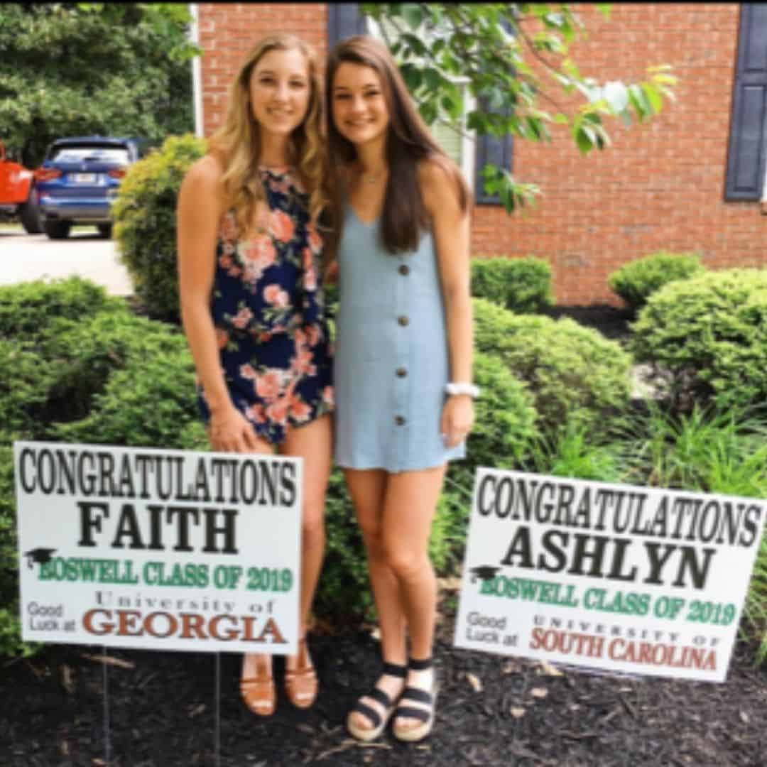 high school senior Faith and Ashlyn in yard with graduation signs